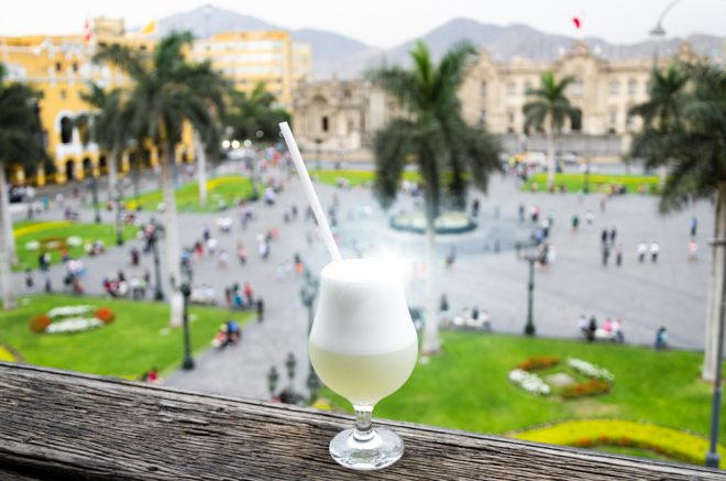 Glass of pisco sour in front of scenic plaza in Peru