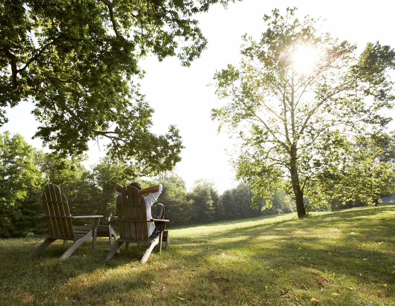 A man relaxes in a wooden chair on a grassy lawn